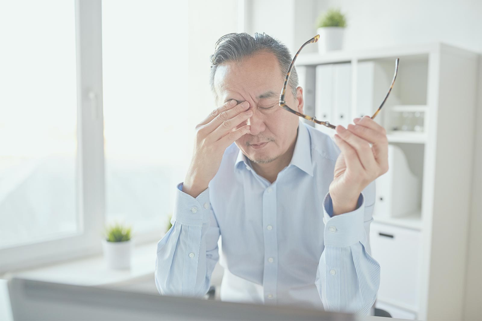 An asian man stressed over his work in his office.